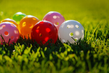 Many light colorful practicing plastic golf balls with holes lays together at green grass. Practicing golf at home lawn. Close up low level photo