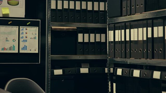 Asian law agent identifying potential missed details mentioned in archived documents, reading folder records to review discrepancies in archive room for investigation. Criminal expertise. Camera B.