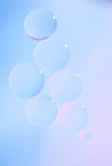 Macro drops of oil on the surface of the water. Delicate cosmetic bubbles background for advertising cosmetic products in soft blue tones, gradient. Vertical photo.