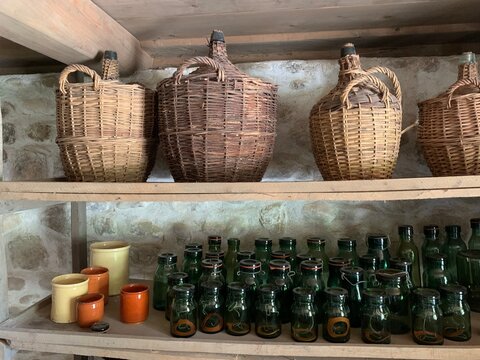 Weinkeller :  Lagerung von Wein in antiken Weink&ouml;rben - geflechtet Winzerweink&ouml;rben im Keller / Gew&ouml;lbekeller darunter alte, gr&uuml;ne Glasflaschen / Weinflaschen als Vorr&auml;te