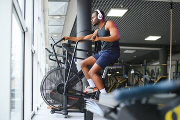 Fototapeta na wymiar Athletic black man doing cardio workout on exercise bike in gym. Concept of sport and healthy lifestyle