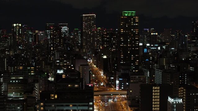 Aerial slide and pan footage of group of tall modern apartment buildings in metropolis. Illuminated wide street in urban borough. Osaka, Japan