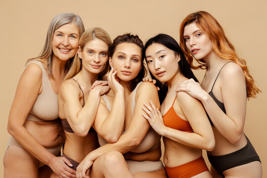 Group portrait beautiful smiling multiethnic women hugging, wearing sexy lingerie isolated on beige background. Attractive stylish fashion models with perfect makeup looking at camera. Natural beauty