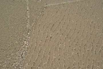 At the beach, gentle ripples caress sand and water, creating a serene and soothing atmosphere