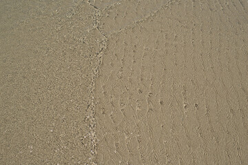 At the beach, gentle ripples caress sand and water, creating a serene and soothing atmosphere