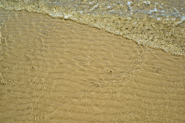 At the beach, gentle ripples caress sand and water, creating a serene and soothing atmosphere