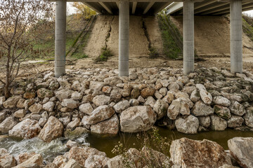 Bottom of a road bridge with a small stream passing underneath surrounded