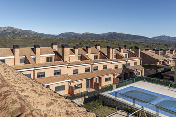 Fototapeta na wymiar An urbanization of semi-detached single-family homes of various heights next to a mountain range with common areas with swimming pools and children's play areas