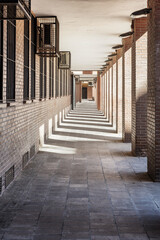 Passage in the basement of a building with shadows of the pillars, vanishing point and air conditioners in metal cages