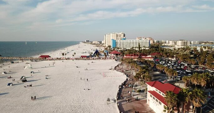 4K high resolution aerial drone video footage of a sandy beach on a sunny day with with some clouds and people, cars, buildings and palm trees in view and a beautiful pier and horizon.