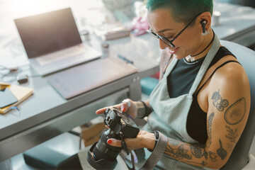 Female designer in eyeglasses looks on shoot in camera screen during working in own design studio
