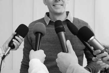 Man giving interview to journalists indoors, closeup. Black and white effect
