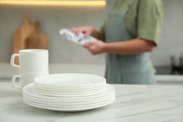 Woman wiping dish with towel in kitchen, focus on stack of plates