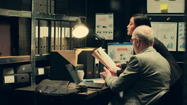 Investigation partners analyze archived autopsy reports and medical records for forensic insights, working in evidence room to gather clues. Law agents team confirm case details. Camera A.