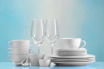 Set of many clean dishware and glasses on light blue table