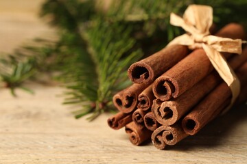 Obraz na płótnie Canvas Bunch of cinnamon sticks and fir branches on wooden table, closeup. Space for text
