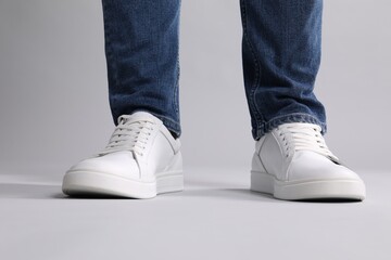 Man wearing stylish white sneakers on grey background, closeup