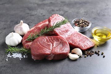 Raw beef steaks, oil and spices on grey table