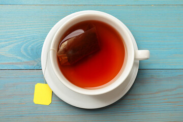 Tea bag in cup with hot drink on light blue wooden table, top view