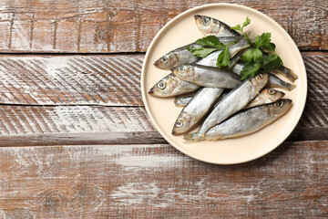 Fresh raw sprats and parsley on wooden table, top view. Space for text