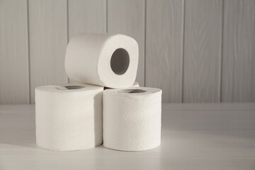 Many soft toilet paper rolls on white wooden table. Space for text