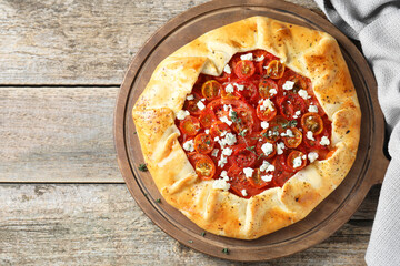 Tasty galette with tomato, thyme and cheese (Caprese galette) on wooden table, top view. Space for text