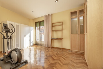 Room with a few closets on the walls, shiny varnished parquet floors and a solitary exercise machine