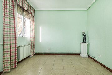 Empty room with walls painted pale green, stoneware floors, a pedestal with a figure lamp and a window with striking curtains on the window