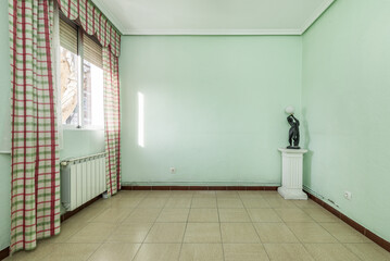 Empty room with walls painted pale green, stoneware floors, a pedestal with a figure lamp and a...