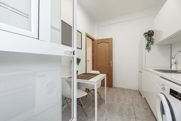 small kitchen furnished with white cabinets, white countertop, white appliances and white square dining table with chairs