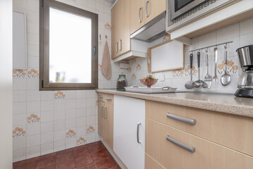Small kitchen furnished with white furniture combined with light wood, aluminum handles, pink copy granite countertop and integrated appliances and a single-leaf window on the wall
