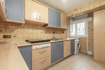 Kitchen furnished with light wood furniture combined with pale blue, aluminum handles, wood-colored countertop and integrated white appliances.