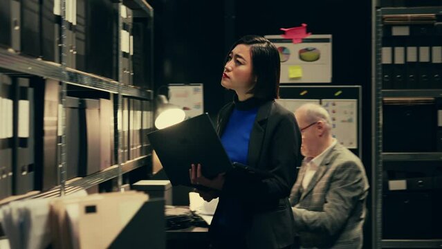 Private investigator searching for old case folders in archive room, comparing witness statements and interviews across multiple investigations. Detective works with classified notes. Camera B.