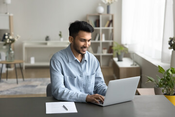 Indian businessman, freelance worker sit at desk with computer, working on-line from home, using laptop, typing message, solve business by e-mailing, correspond to client, do task. Workflow using tech