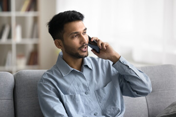 Serious Indian man talk to customer services receive helpful information by phone call. Single guy...