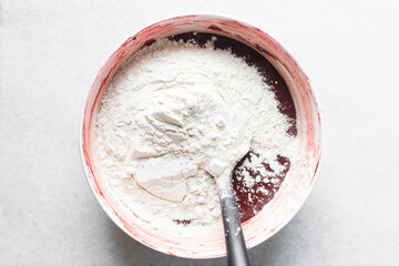 flour being mixed into red velvet brownie batter in a white mixing bowl, overhead view of red velvet fudge brownie batter in a white ceramic mixing bowl