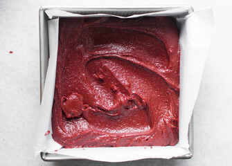 red velvet brownie batter in a parchment lined baking tray, overhead view of red velvet fudge...