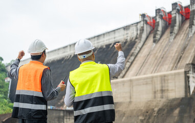 Fototapeta premium Confident asian two maintenance engineers man inspection discussstion with tablet at construction site dam with hydroelectric power plant and irrigation. Team engineer man working at project