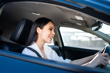 Young beautiful asian business women getting new car. She very happy and excited. Smiling female driving vehicle on the road on a bright day with sun light. Business woman buying driving new car