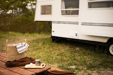 Tin tourist mug with cocoa, marshmallow on sticks for making smore, basket with food and a plaid on a wooden table in a travel trailer park. Dessert on a hike.