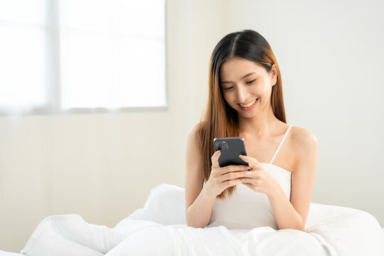 Pretty asian woman using smart phone on bed to social media at home in the morning. Lifestyle of young beautiful female using mobile phone to network internet online on the bed