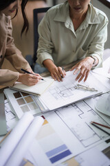 Two female architects discuss about interior design building project on blueprint and taking notes - 744940831