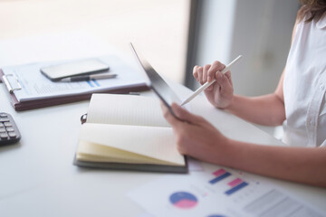 Fototapeta premium Asian businesswomen reading marketing business report on digital tablet and finance document of new business to taking notes while analyze investment and market stock of new startup in outside office