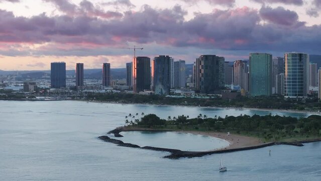 Modern buildings of Ala Moana area at cinematic sunset. Scenic Ala Moana beach on Magic island, Oahu Hawaii 4K USA. Pastel lilac pink purple clouds above Kaka Ako district in modern Honolulu downtown