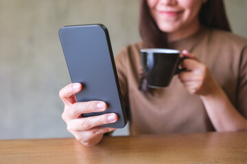 Closeup image of a young woman holding and using mobile phone while drinking coffee