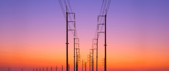 Silhouette two rows of electric poles with cable lines on curve road against colorful twilight sky...