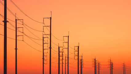 Silhouette rows of electric poles with cable lines against colorful orange sunset sky background,...