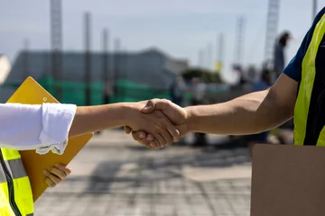 Fotobehang Handshaking of engineer in reflective clothing for industrial business deal and partnership agreement contract with ongoing construction in the background © Akarawut