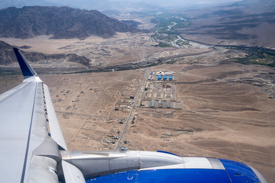 Airplane Window view of plane wings in the foreground and mountain view in the background with airport in the middle