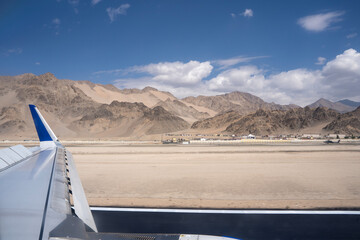 A shot from airplane window, visible plane wings. Dry Mountains with runway in the foreground and...
